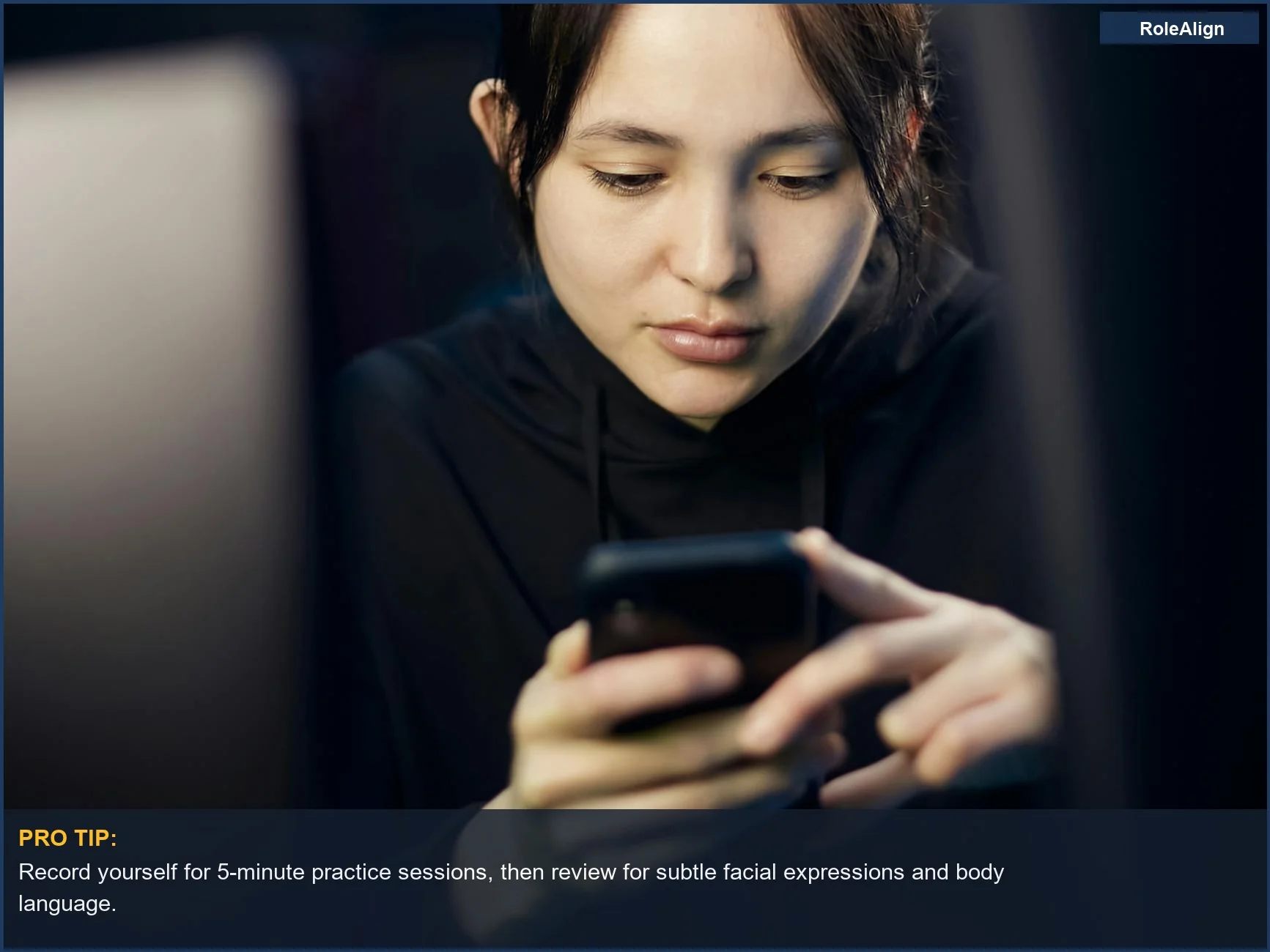 Mujer mirando atentamente un teléfono inteligente en interiores, demostrando el análisis detallado de señales no verbales por parte de herramientas de preparación de entrevistas con IA.