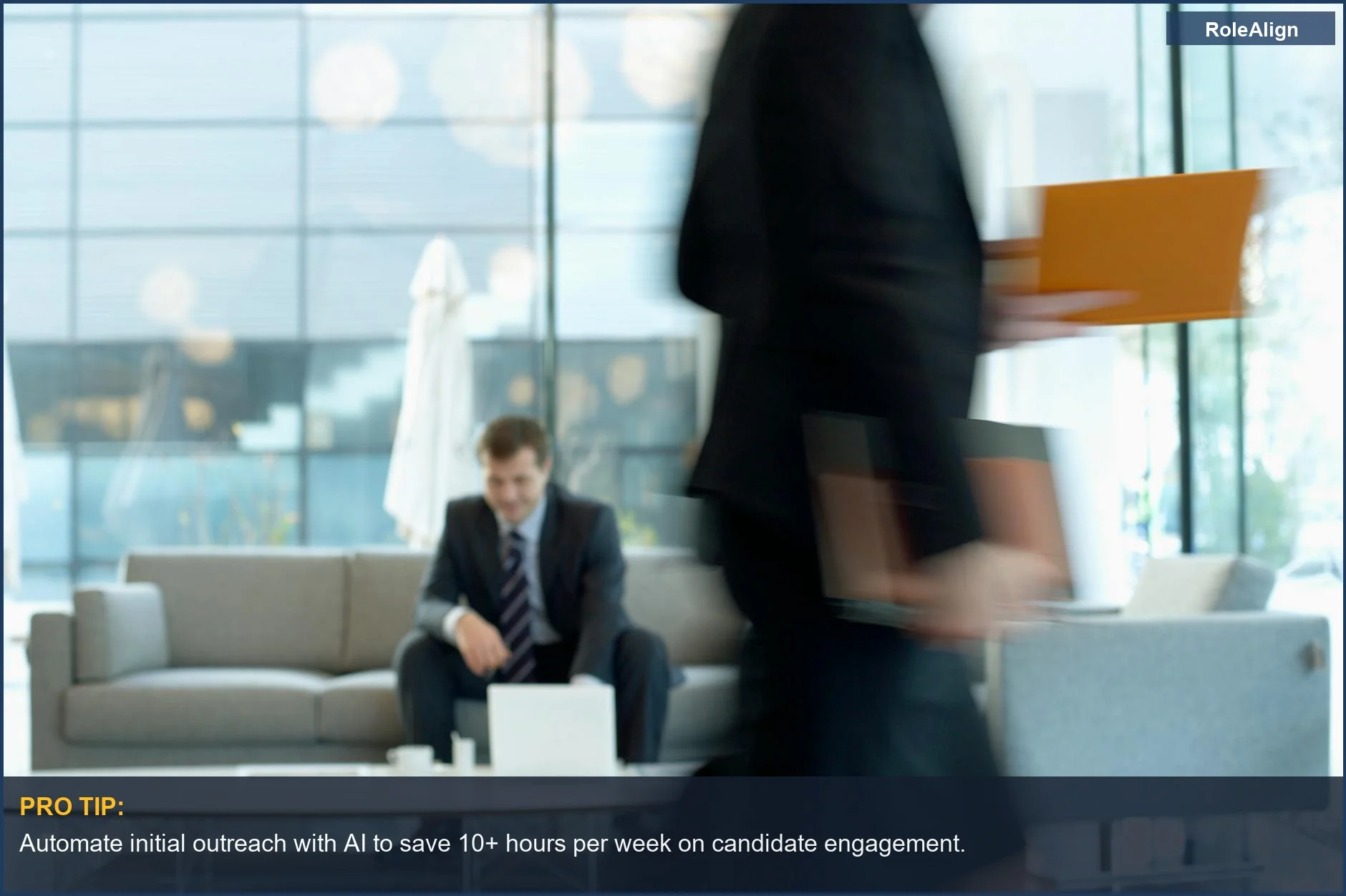 Businessman in a modern office lounge using a laptop with a colleague blurring in the background, symbolizing AI workflow.