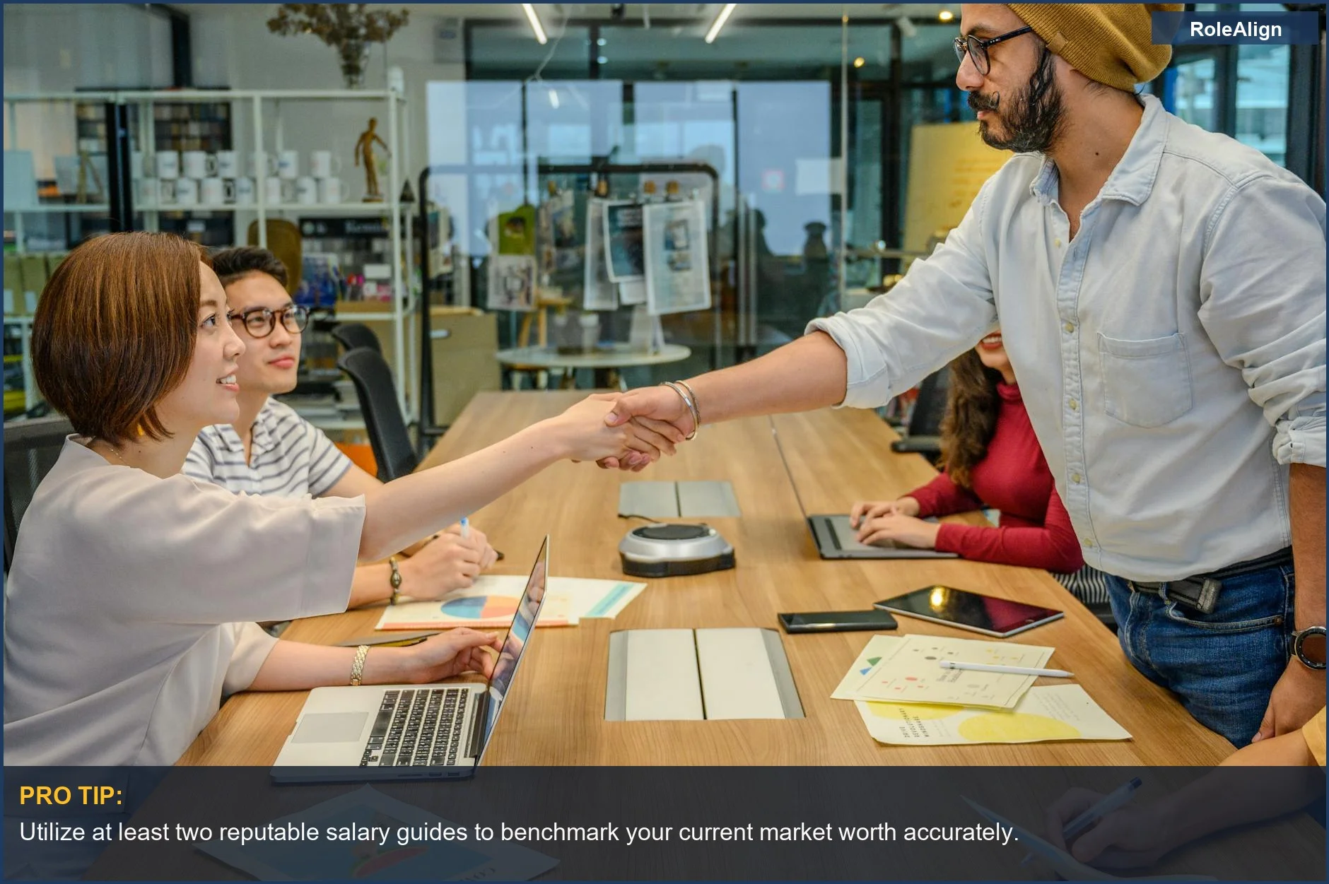 Professionals shake hands in a modern office, illustrating the collaborative effort needed to research market value for a salary raise.