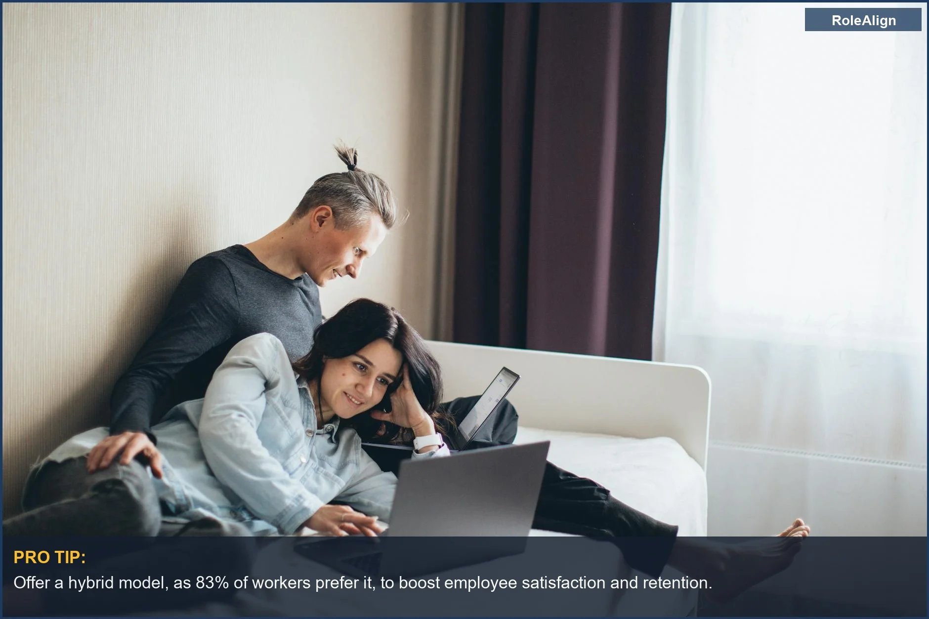 Happy couple working together on laptops in a cozy home bedroom, illustrating the benefits of hybrid work.