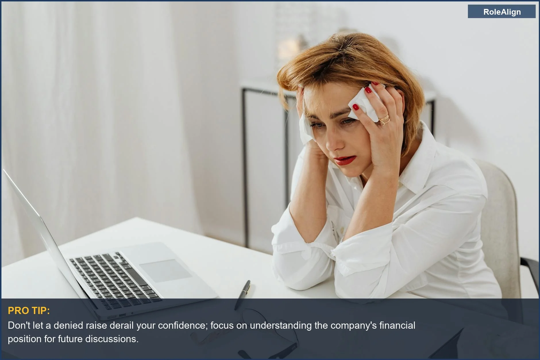 Woman looking distressed at office desk after raise rejected, surrounded by tissues.