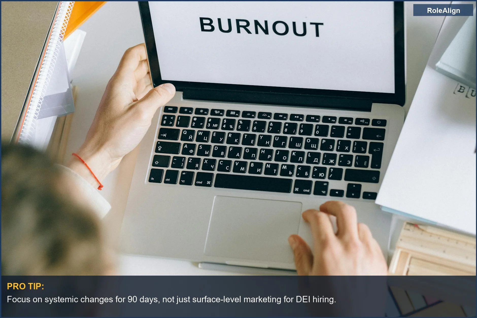 Overhead view of person typing 'BURNOUT' on laptop, highlighting diversity hiring problems.