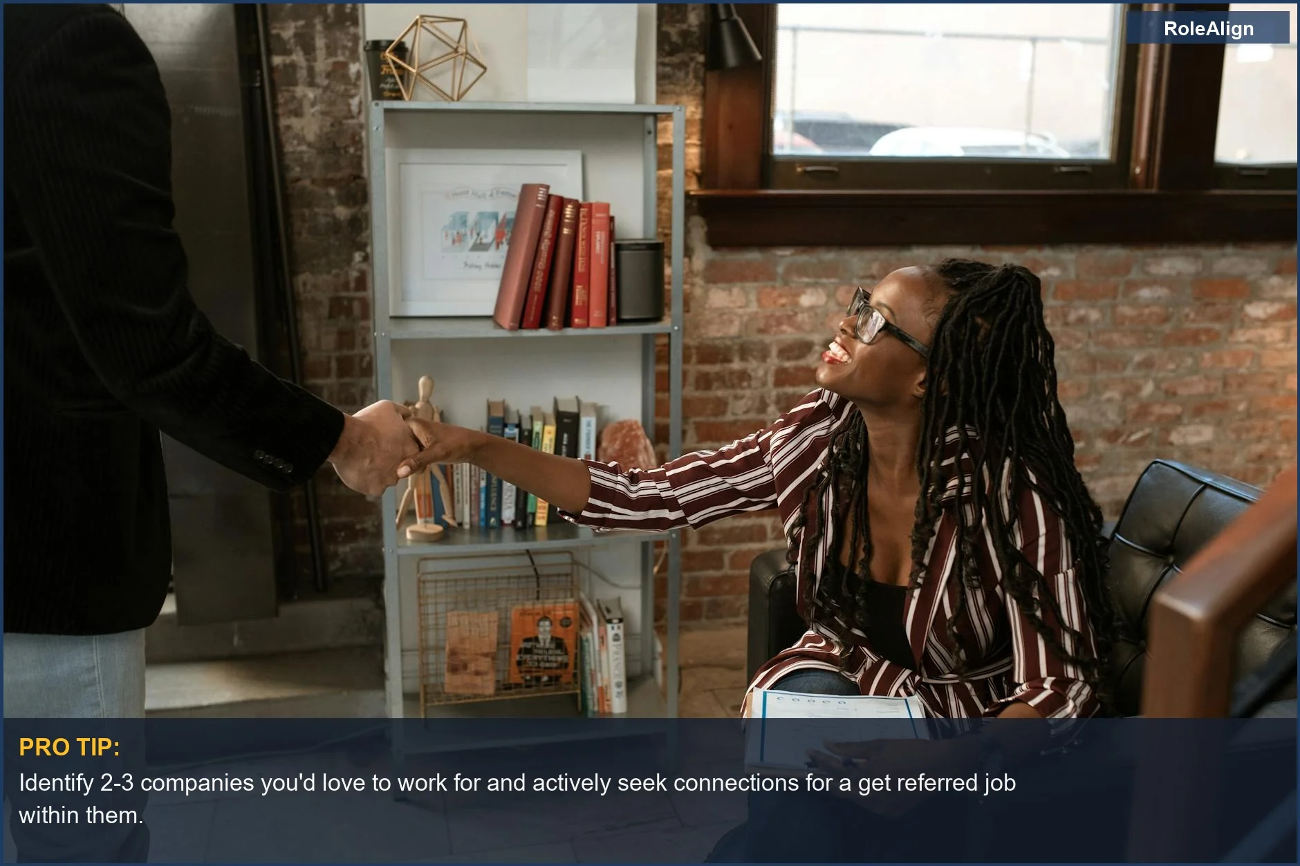 Smiling woman in a striped shirt shaking hands with a colleague in a warm office, highlighting a successful get referred job connection.