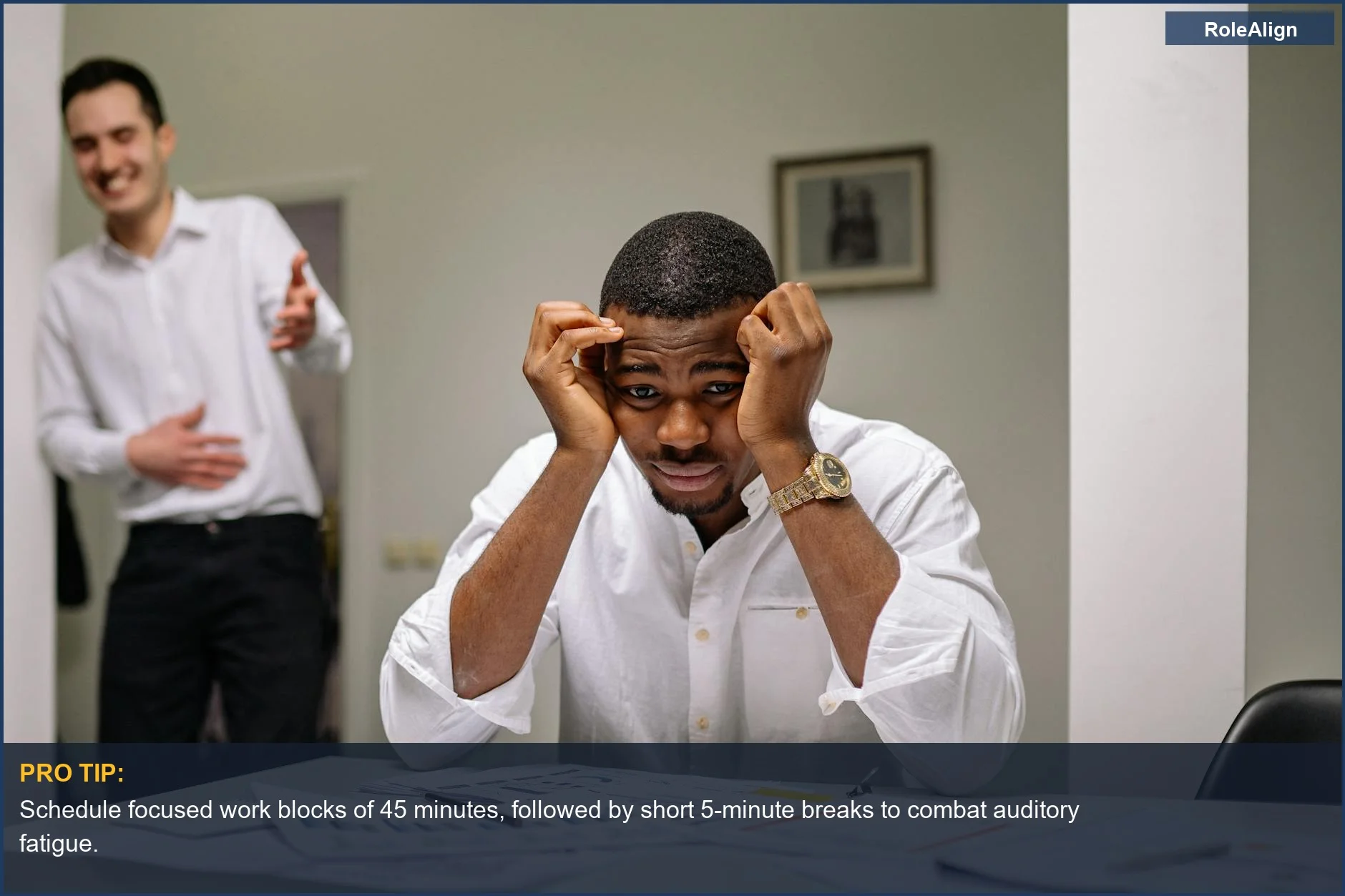 Tensed businessman at desk with a laughing coworker nearby, demonstrating the impact of open office noise on focus.