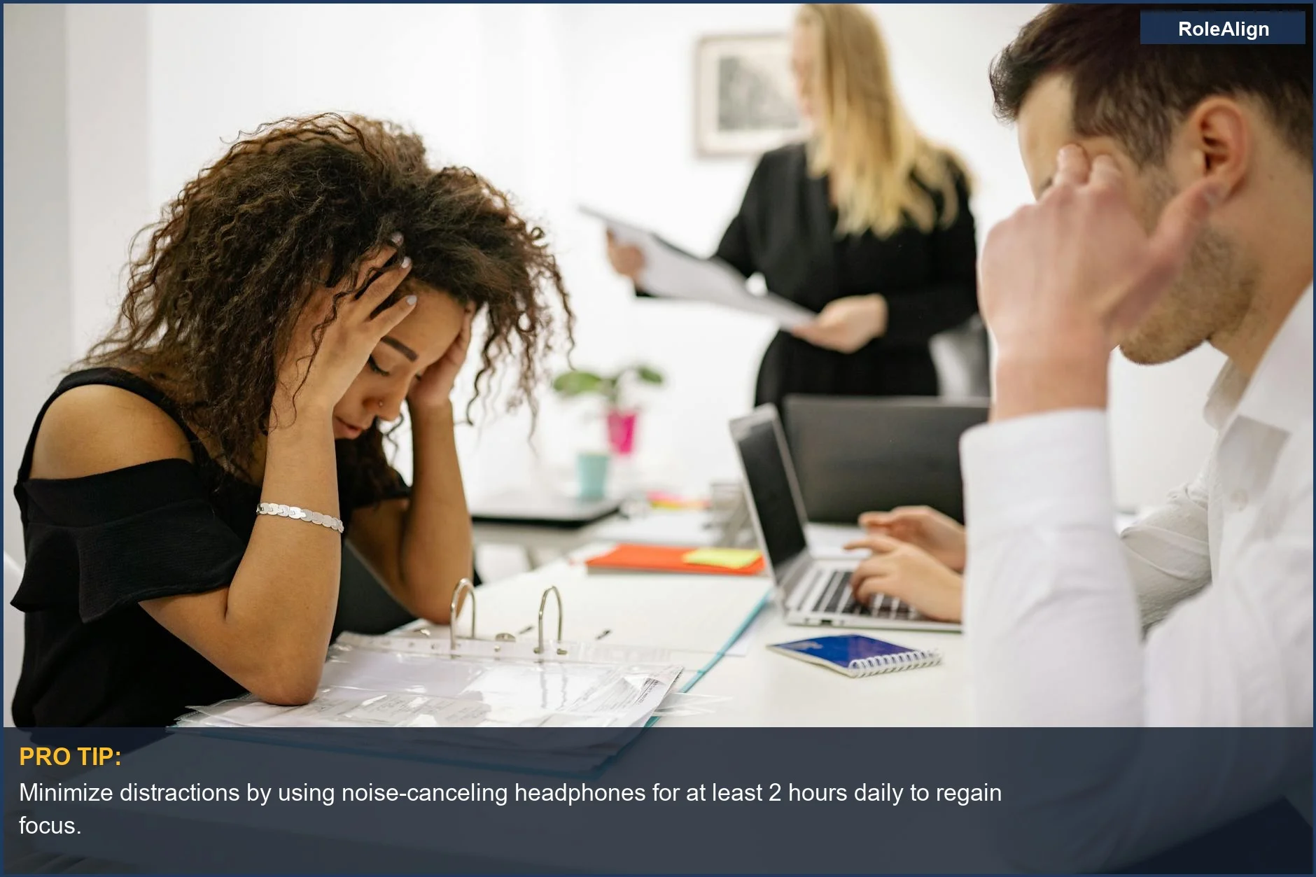 African American woman overwhelmed at open office desk, highlighting open office productivity challenges and workplace pressure.