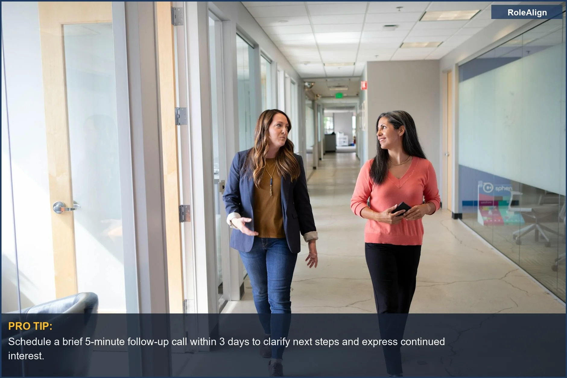 Two professional women discussing in a modern office corridor, a visual for understanding how recruiters avoid ghosting.