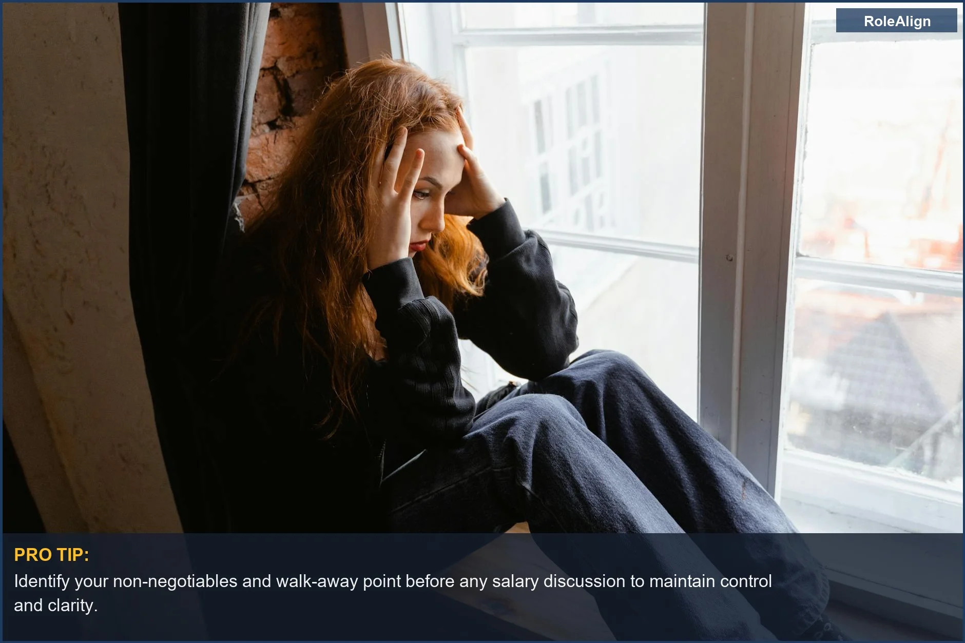 Woman in deep thought by window, conveying distress about salary negotiation psychology.