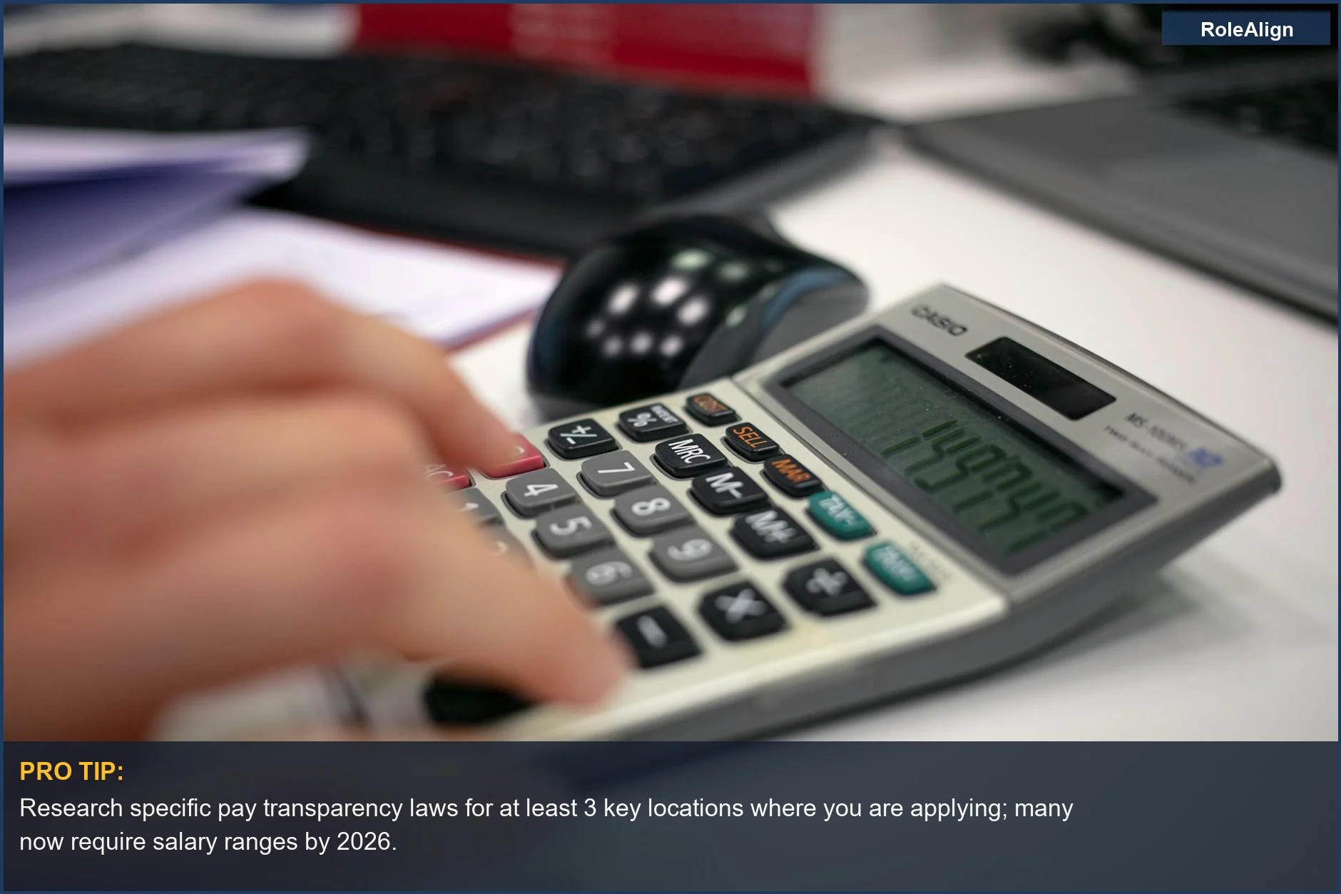 Hand using a calculator on an office desk, emphasizing the need to research pay transparency laws for salary ranges.