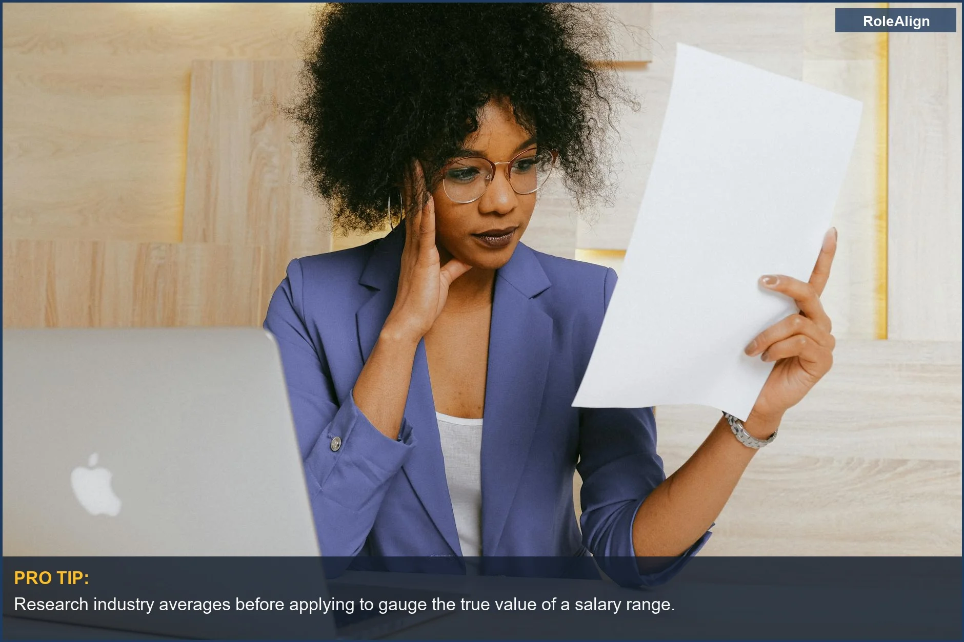 Businesswoman reviewing a document while working on a laptop, illustrating job posting salary range opacity.