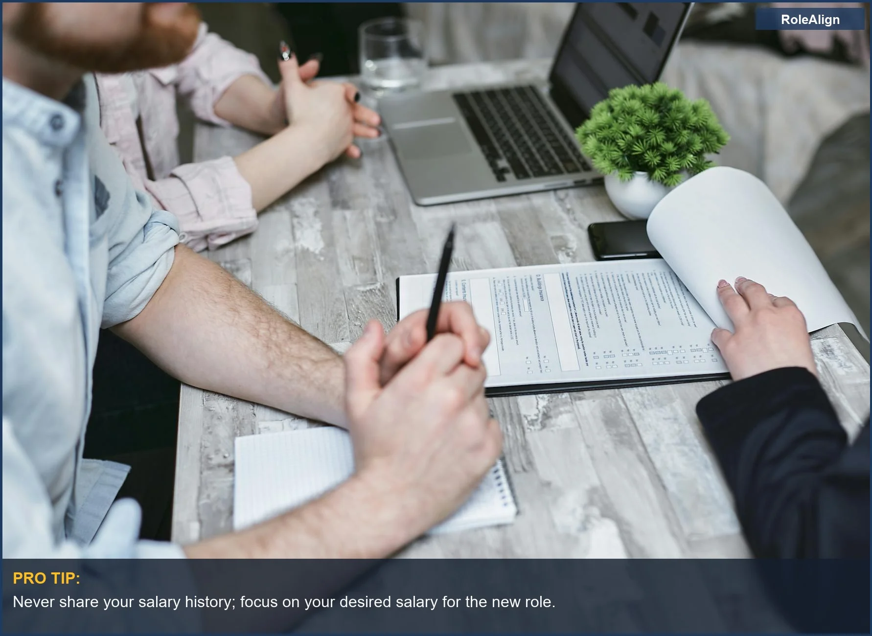 Business meeting with laptop and documents on table, discussing salary history with recruiters.